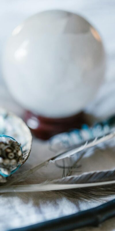 A spiritual arrangement featuring a crystal ball, sage bundle, and feathers, ideal for mystical themes.
